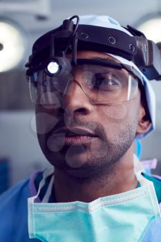 Portrait Of Male Surgeon Wearing Protective Glasses And Head Light In Hospital Operating Theater