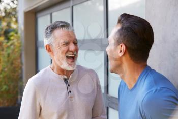Senior Hispanic Man Talking And Laughing With Adult Son In Garden At Home