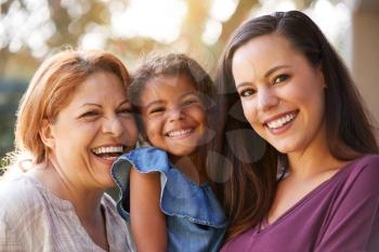 Portrait Of Multi-Generation Female Hispanic Family In Garden Smiling At Camera