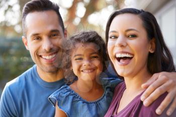 Portrait Of Smiling Hispanic Family With Daughter Laughing In Garden At Home