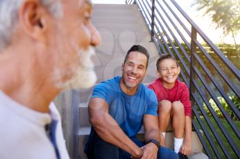 Smiling Multi-Generation Male Hispanic Family Sitting On Steps In Garden And Talking Together