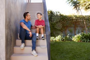 Smiling Hispanic Father And Son Sitting On Steps In Garden Talking Together