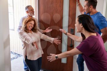 Couple Greeting Senior Parents At Front Door As They Come To Visit