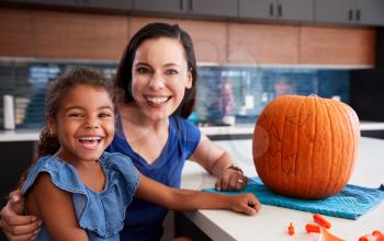 Portrait Of Mother And Daughter Carving Halloween Lantern From Pumpkin At Home