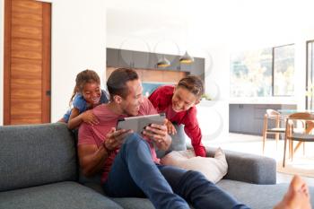 Children Creeping Up And Surprising Father Using Digital Tablet At Home