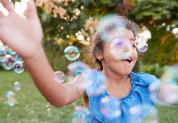 Young Hispanic Girl Chasing And Catching Bubbles In Garden