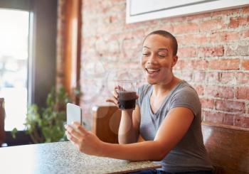 Woman Making Video Call On Mobile Phone Sitting In Coffee Shop