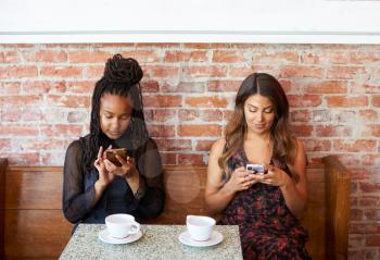 Female Customers Using Mobile Phones Sitting In Coffee Shop