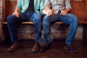 Close Up On Feet Of Same Sex Male Couple Holding Hands Sitting On Bench Together