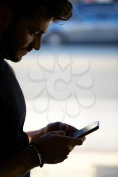 Silhouette Of Man Texting On Mobile Phone Standing By Window