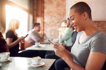 Woman Using Mobile Phone Sitting At Table In Coffee Shop