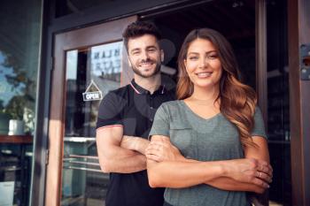Portrait Of Couple Starting New Coffee Shop Or Restaurant Business Standing In Doorway