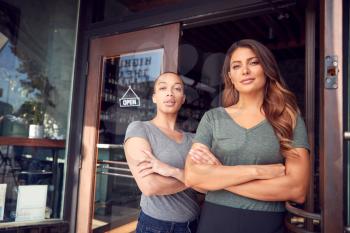 Portrait Of Two Women Starting New Coffee Shop Or Restaurant Business Standing In Doorway