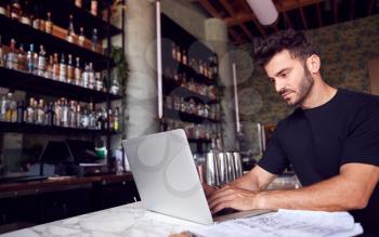 Male Owner Of Restaurant Bar Sitting At Counter Working On Laptop