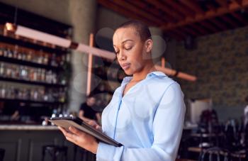 Confident Female Owner Of Restaurant Bar Standing By Counter Holding Digital Tablet