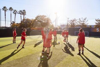 Womens Football Team Kicking Ball Whilst Training For Soccer Match On Outdoor Astro Turf Pitch