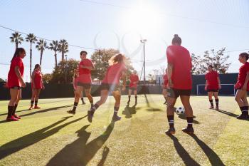 Womens Football Team Kicking Ball Whilst Training For Soccer Match On Outdoor Astro Turf Pitch