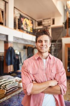Portrait Of Smiling Male Owner Of Fashion Store Standing In Front Of Clothing Display