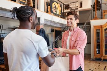 Sales Assistant Handing Purchases To Male Customer In Fashion Store