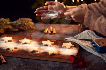 Hand Shaking Icing Sugar Over Baked Star Shaped Christmas Cookies On Board Ready For Decoration