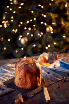 Traditional Christmas Panettone On Table Set For Festive Meal With Tree Lights In Background