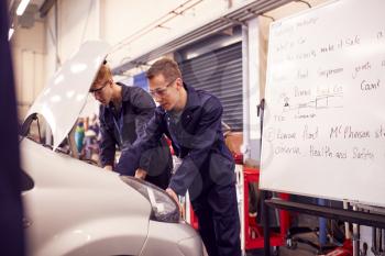 Two Male Students Studying For Auto Mechanic Apprenticeship At College Working On Car Engine