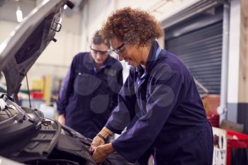 Female Tutor With Students Looking At Car Engine On Auto Mechanic Apprenticeship Course At College