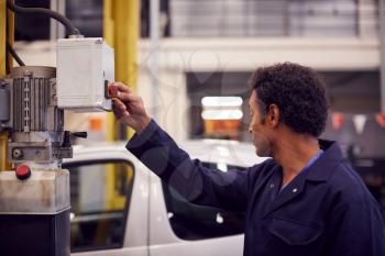 Male Motor Mechanic Raising Car On Hydraulic Lift In Garage