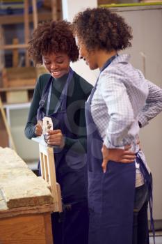 Tutor With Female Carpentry Student In Workshop Studying For Apprenticeship At College Planing Wood