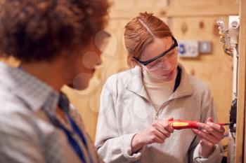 Female Tutor With Trainee Electrician In Workshop Studying For Apprenticeship At College