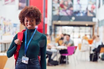 Portrait Of Smiling Female College Student In Busy Communal Campus Building