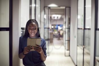 Evening Shot Of Businesswoman Standing In Corridor Of Modern Office Using Digital Tablet