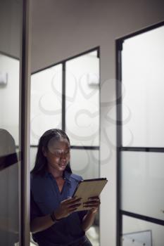 Evening Shot Of Businesswoman Standing In Corridor Of Modern Office Using Digital Tablet