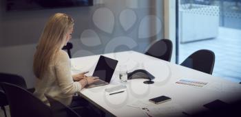 Businesswoman Working Late In Office Meeting Room Using Laptop