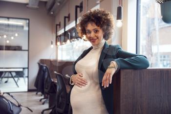 Portrait Of Pregnant Businesswoman Holding Bump Working In Modern Office
