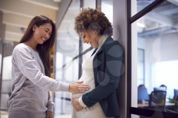 Businesswoman Touching Pregnant Female Colleagues Bump In Modern Office