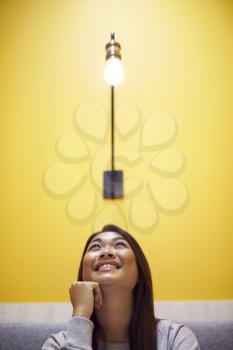 Woman Sitting Under Light Bulb In Office Suggesting Inspiration Or Idea