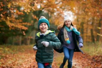 Two Smiling Children Having Fun Running Along Path Through Autumn Woodland Together