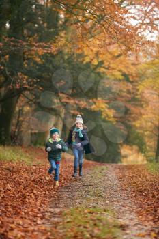 Two Smiling Children Having Fun Running Along Path Through Autumn Woodland Together