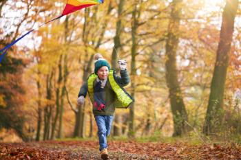 Young Boy Having Fun Running Along Path Through Autumn Woodland Flying Kite