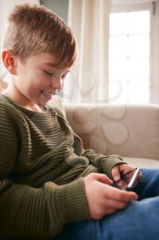 Young Boy On Sofa At Home Having Fun Playing Game On Mobile Phone