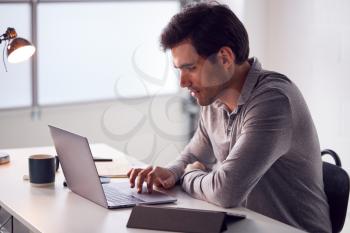 Businessman Working On Laptop At Desk In Modern Office
