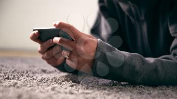 Close Up Of Woman At Home Looking At Social Media And Text Messages On Mobile Phone Lying On Carpet