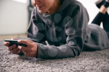 Close Up Of Woman At Home Looking At Social Media And Text Messages On Mobile Phone Lying On Carpet