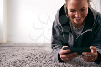 Woman Relaxing At Home Looking At Social Media And Text Messages On Mobile Phone Lying On Carpet