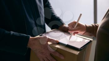 Woman Signing For Courier Delivery To Office Using Digital Tablet
