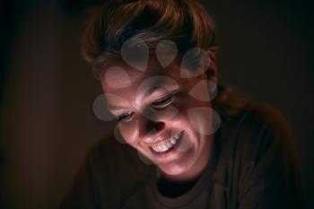 Smiling Woman With Face Illuminated By Digital Tablet Screen At Night