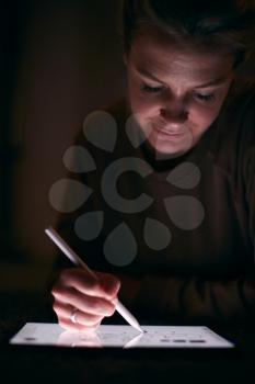 Close Up Of Woman Drawing On Digital Tablet Using Stylus Pen Lying On Carpet At Night