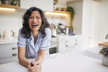 Portrait Of Smiling Mature Hispanic Woman Wearing Pyjamas Spending Morning At Home In Kitchen
