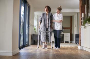 Mature Woman In Dressing Gown Using Walking Frame Being Helped By Female Nurse